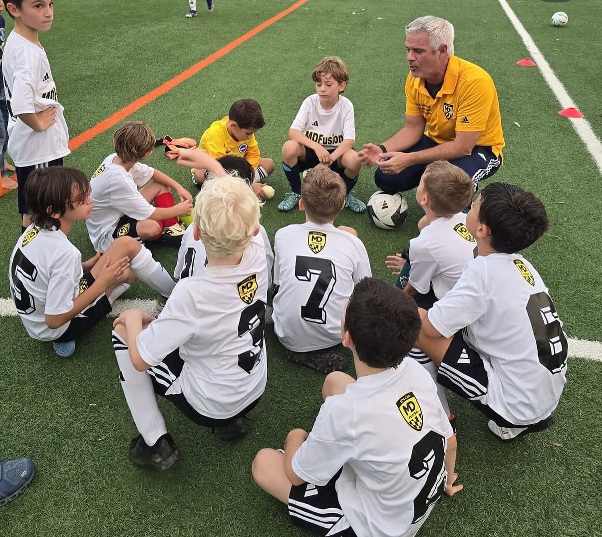 An MD Fusion coach kneeling with a group of players during a tactical talk